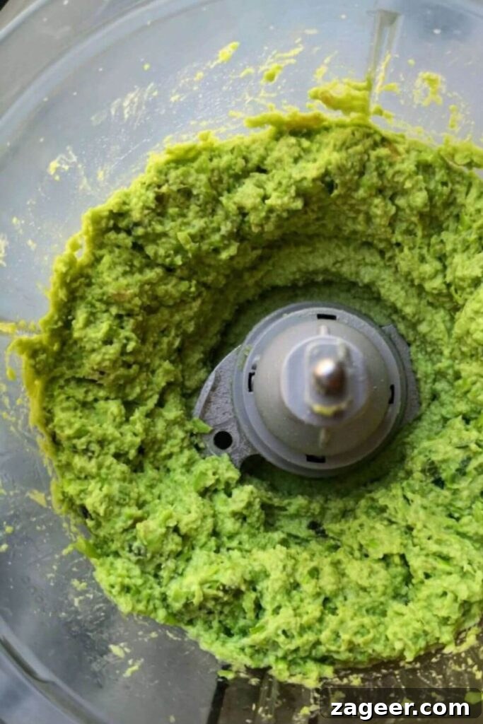 Vibrant Edamame Avocado Hummus 5 Edamame hummus with avocado blitzed up in the bowl of a food processor.