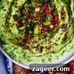 Edamame hummus with avocado on a small white plate, with pita chips on the side.