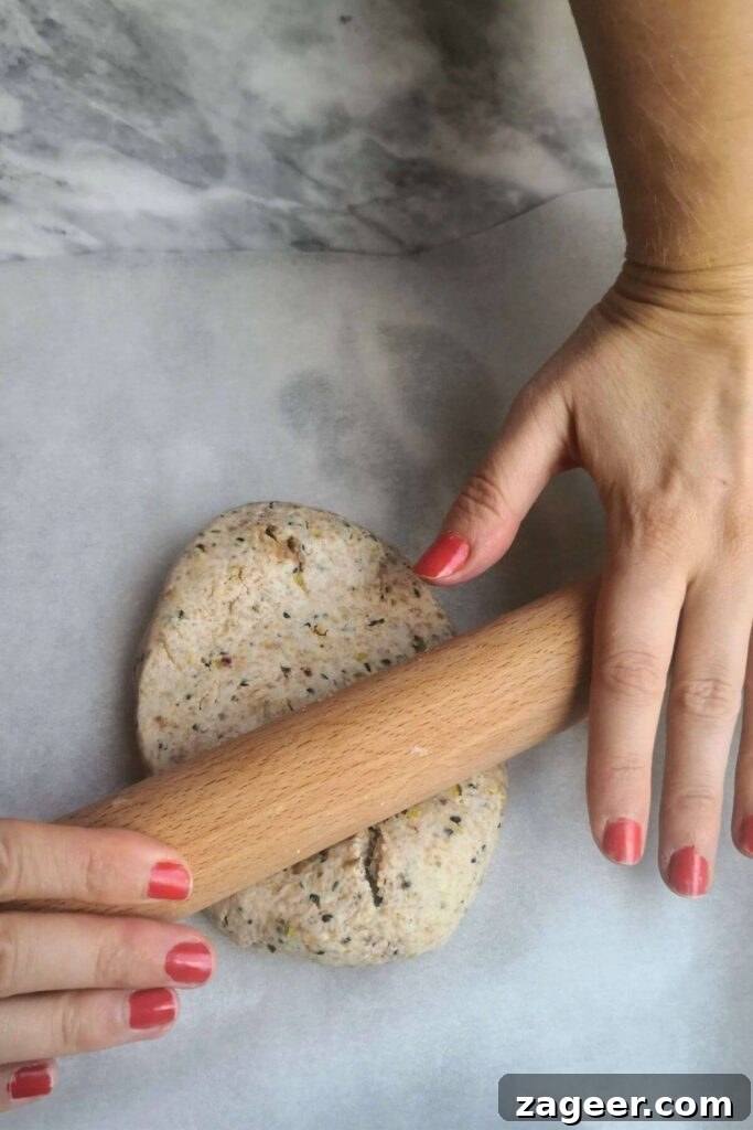 Tangy Sourdough Crisps with Aromatic Dukkah 6 Hands expertly rolling out sourdough discard dough with a wooden rolling pin directly onto a sheet of baking paper.