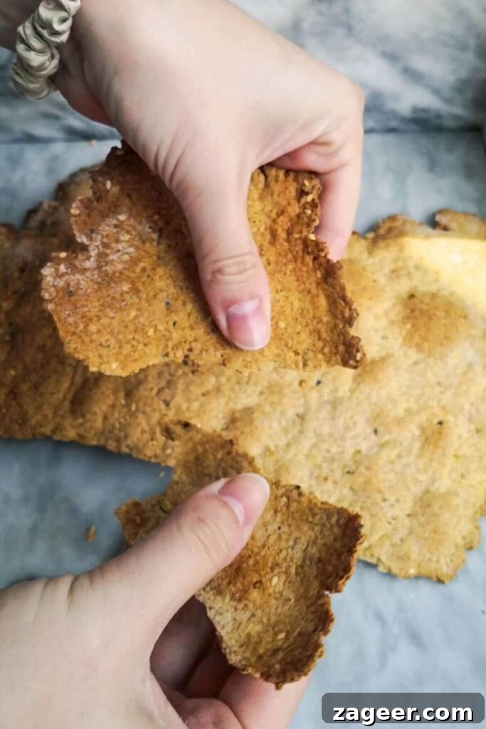 Tangy Sourdough Crisps with Aromatic Dukkah 9 Hands gently breaking the cooled sourdough cracker sheet into smaller, irregular pieces, showcasing their rustic appeal.