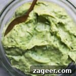Green tahini sauce in a small glass bowl with a gold spoon inside, on a grey marble background.