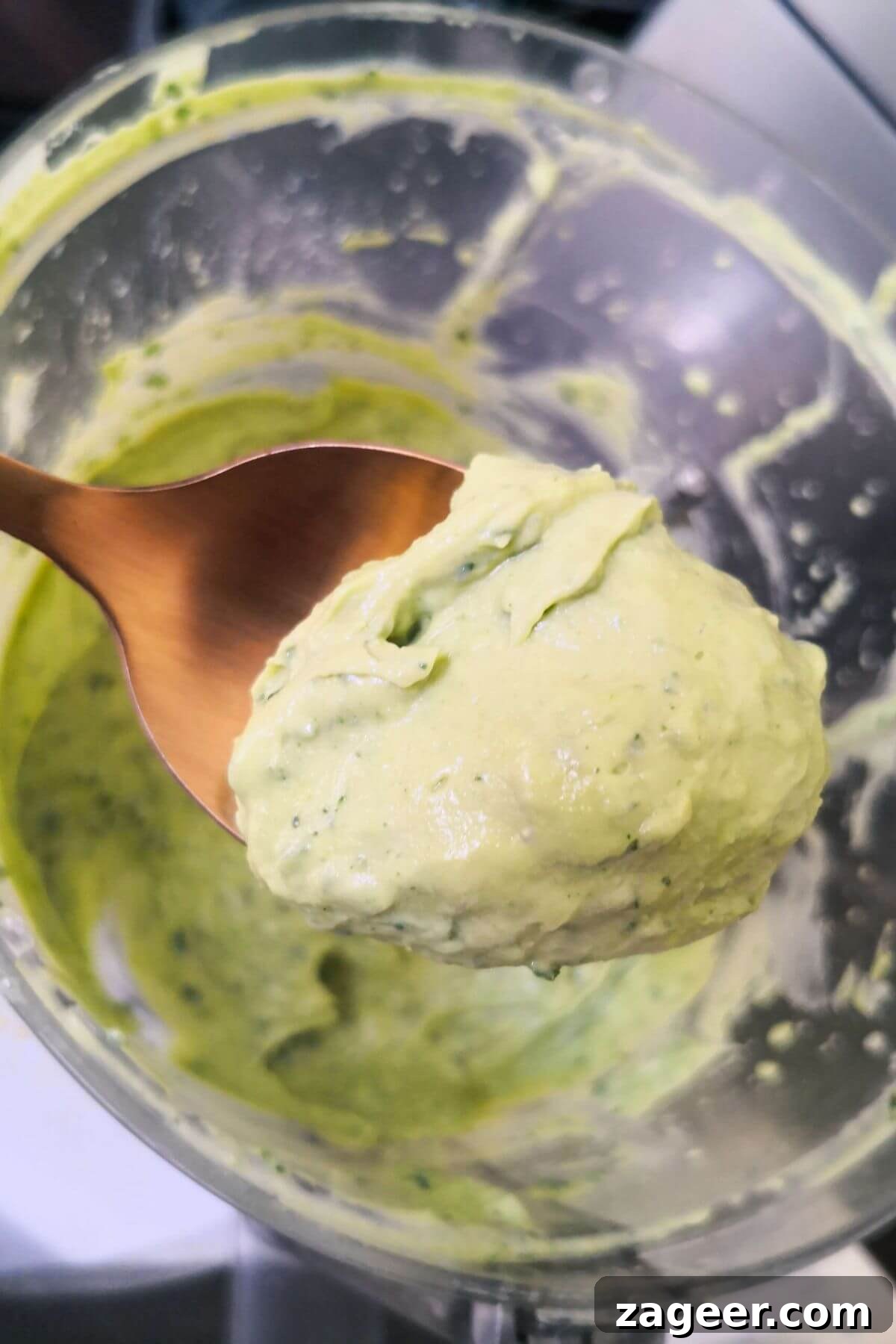 Vibrant 5-Minute Vegan Green Tahini Sauce 6 Close up of spoon with green tahini on it, with food processor bowl in the background.