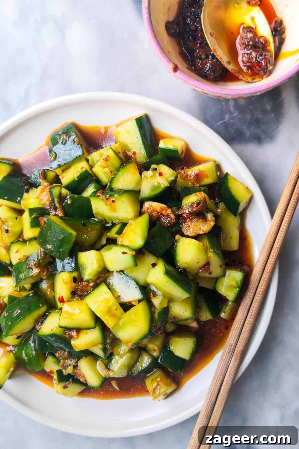 Smacked cucumber salad on a white plate with chopsticks on the side, with a small bowl of chilli oil.