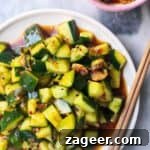 Smacked cucumber salad on a white plate with chopsticks on the side, with a small bowl of chilli oil.