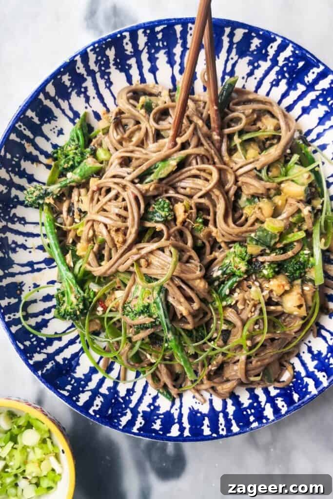 Emerald Goddess Chopped Salad Craze 12 Sesame soba noodles with cucumber and broccolini in a white and blue bowl with chopsticks, with a small bowl of spring onions on the side.