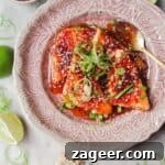 Four wedges of sweet chilli haloumi on a pink plate with more sweet chilli on the side, garnished with spring onion and sesame seeds.
