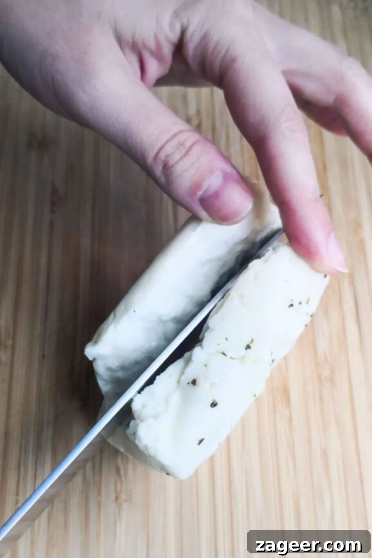 Sticky Sweet Chili Halloumi 4 Chopping halloumi block in half on a wooden board.