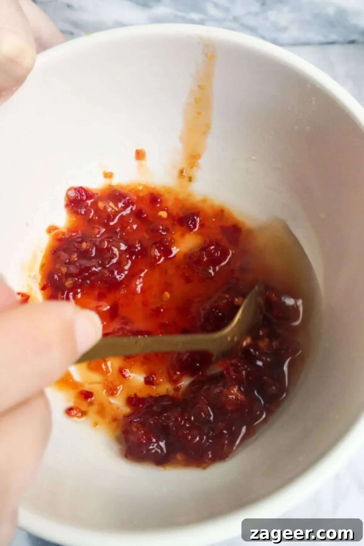 Sticky Sweet Chili Halloumi 6 A hand holding a gold spoon mixing chilli jam and lime juice in a small white bowl.
