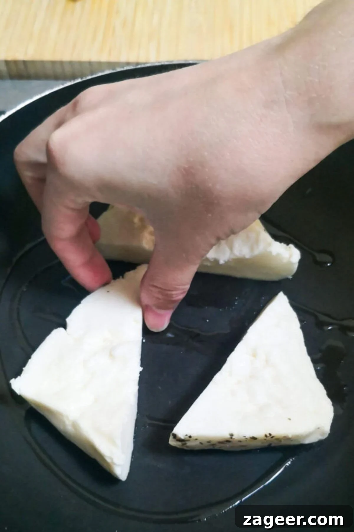 Sticky Sweet Chili Halloumi 7 A hand placing halloumi triangles in a small black pan.