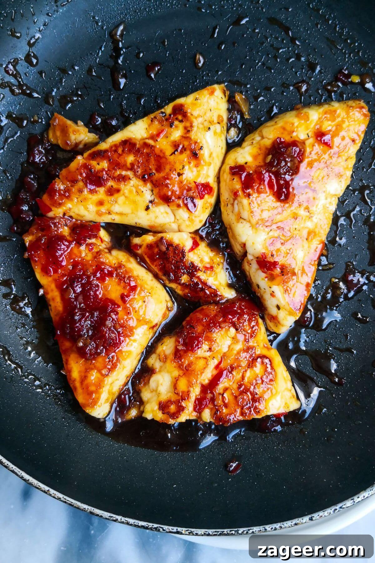 Sticky Sweet Chili Halloumi 8 5 golden sweet chilli jam glazed halloumi triangles in a small black pan, simmering in the sauce.