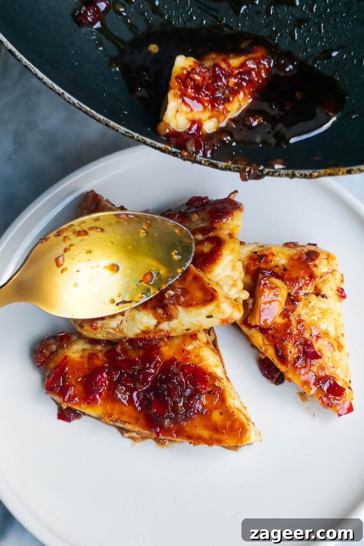 Sticky Sweet Chili Halloumi 9 Sweet chilli glazed halloumi triangles being transferred from a small black pan to a white serving plate with a gold spoon.