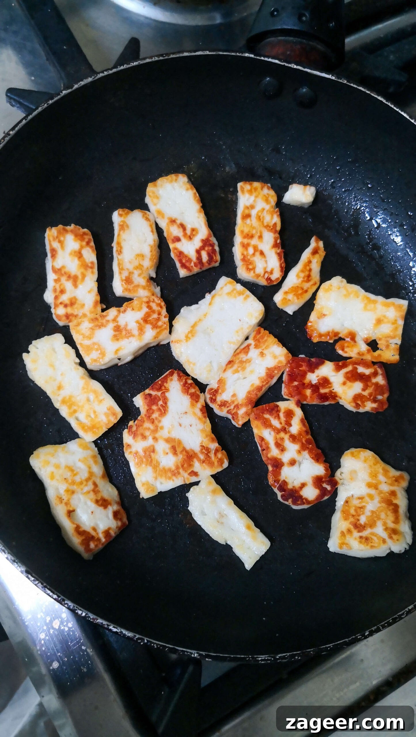 Sweet & Salty Peach Halloumi Salad with Chili Jam 7 Perfectly golden halloumi slices sizzling in a small black pan, showcasing the delicious crispiness achieved during cooking.