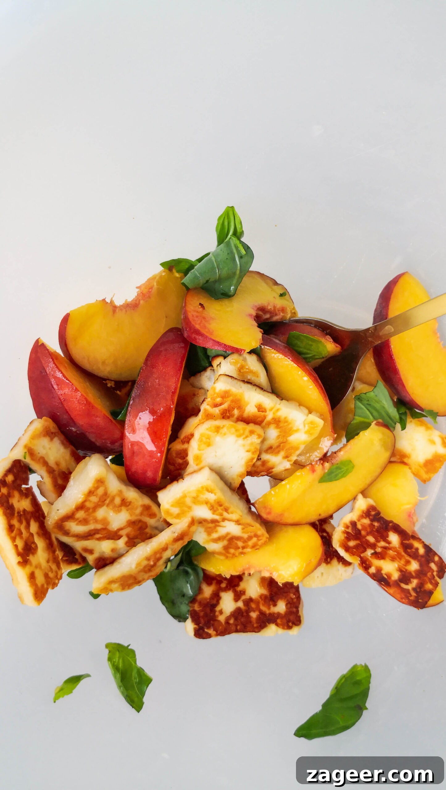 Sweet & Salty Peach Halloumi Salad with Chili Jam 8 Vibrant peach and halloumi salad being gently mixed in a large, clear bowl, ensuring all ingredients are well combined and coated.