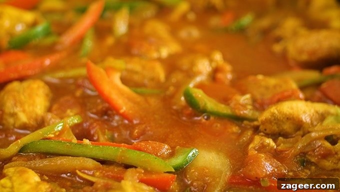 Vibrant Spicy Chicken Jalfrezi 7 Close-up view of Chicken Jalfrezi simmering in a pan, showcasing the rich, thick, and spicy tomato-based sauce with tender chicken and colorful peppers.