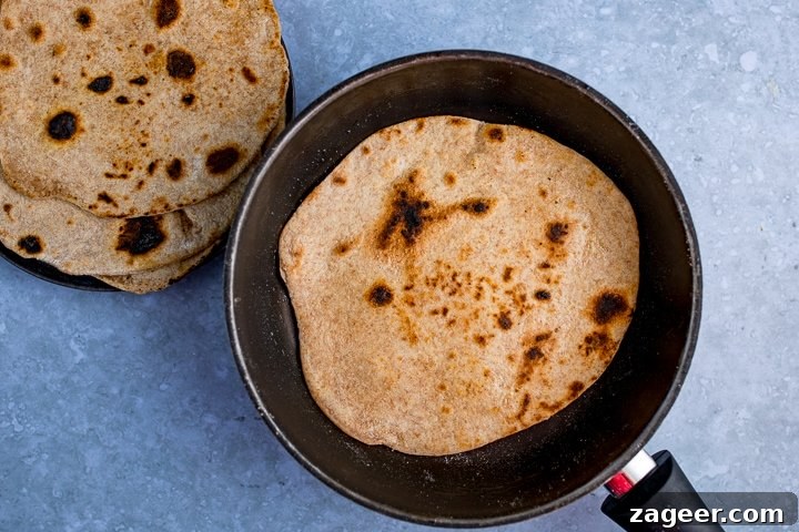 Perfect Homemade Chapati 5 A freshly rolled chapati frying in a hot pan, showing the beginning of charred spots and a slight puff.