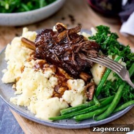 Slow cooker short ribs with rich gravy served elegantly on a bed of creamy mashed potatoes, accompanied by fresh green vegetables.