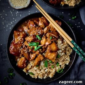 Close-up shot of honey garlic chicken, glistening with sauce, served with white rice and fresh greens, ready to eat.