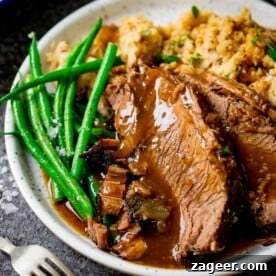 Plate of perfectly sliced roast beef, accompanied by vibrant vegetables and a generous pour of rich gravy, all presented on a dark background.