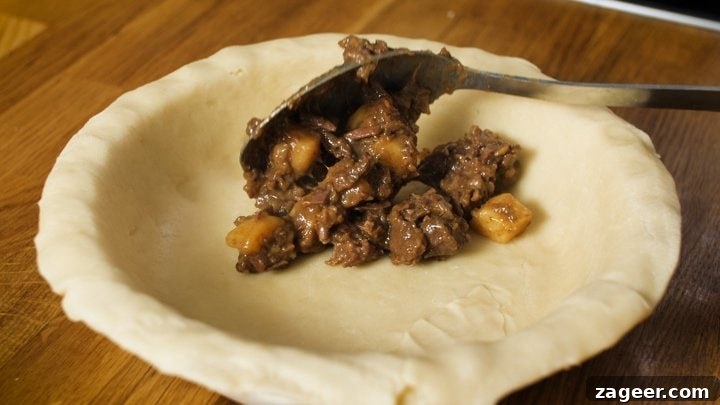 Melt-in-Your-Mouth Slow-Cooked Steak Pie 7 Steak and potato filling being carefully spooned into a pastry-lined pie dish.
