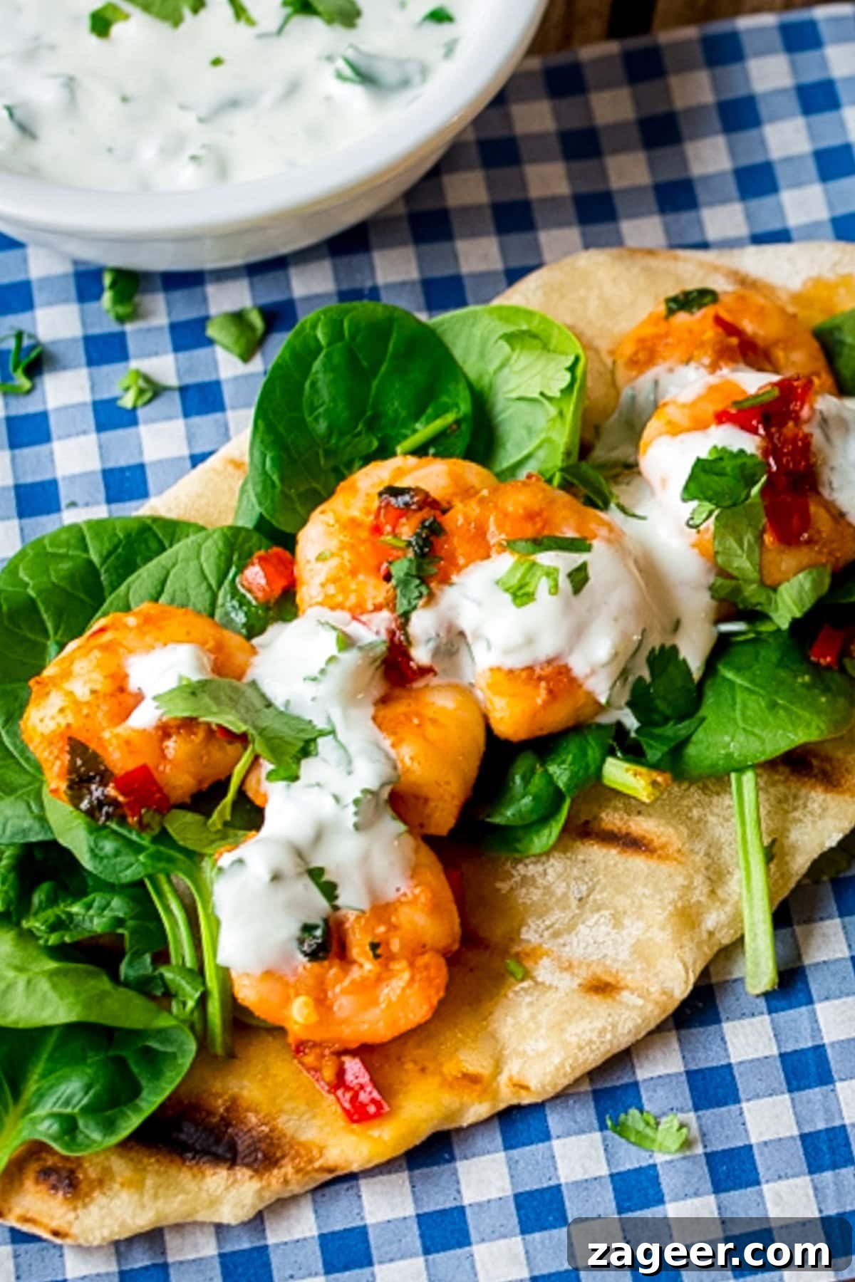 Spicy Garlic Prawns with Quick Flatbreads and Cooling Yogurt Dip 2 Tall image of Garlic chilli prawns with spinach and yogurt dip on homemade flatbread on a piece of blue chequered paper. This quick shrimp recipe is perfect for easy weeknight dinners.