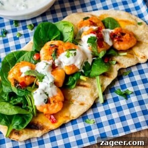 Garlic chilli prawns with spinach and yogurt dip on homemade flatbread on a piece of blue chequered paper. A full dish ready to serve.