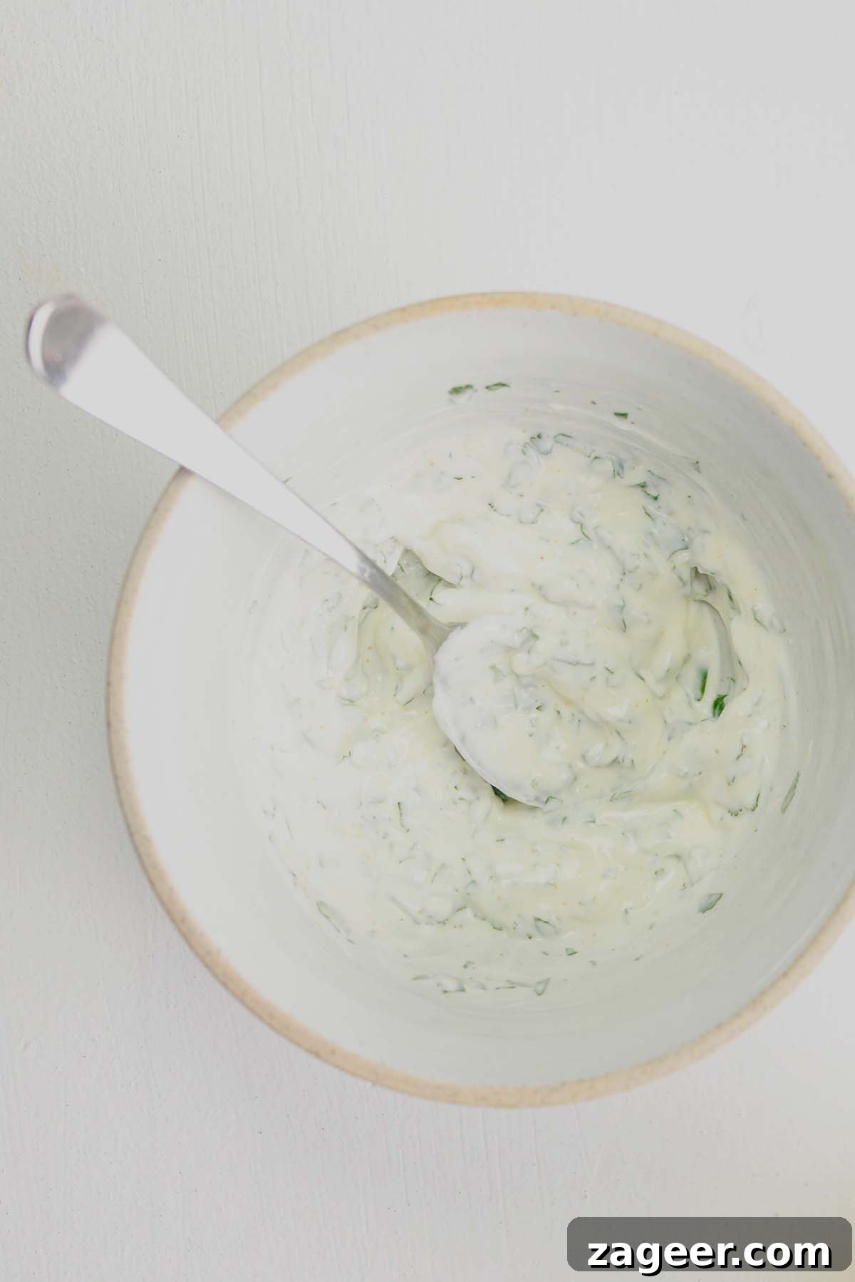 Spicy Garlic Prawns with Quick Flatbreads and Cooling Yogurt Dip 3 Overhead image of yogurt dip in a white bowl on a white surface, showcasing the creamy texture and fresh herbs.