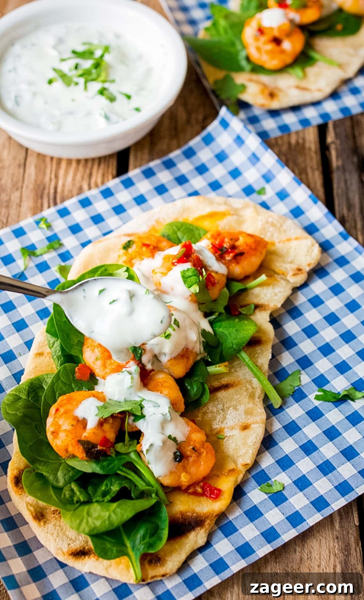Spicy Garlic Prawns with Quick Flatbreads and Cooling Yogurt Dip 6 Spoonful of yogurt dip being drizzled on garlic chilli prawns with spinach on homemade flatbread on a piece of blue chequered paper. A delightful, quick shrimp meal.