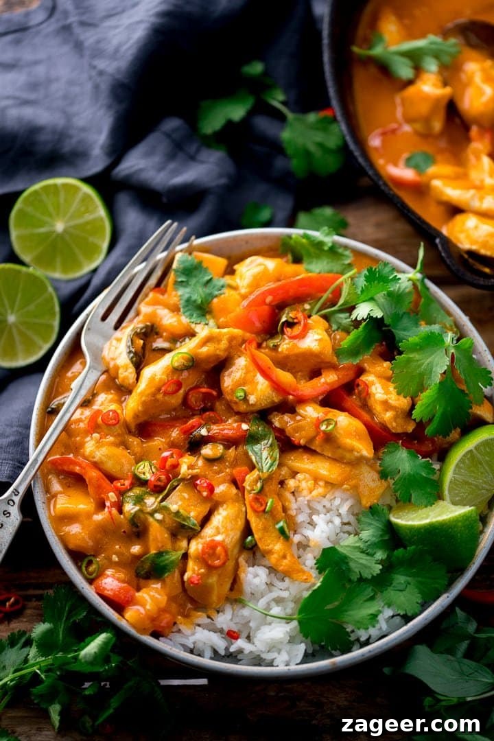 Vibrant Thai Red Chicken Curry 2 A steaming bowl of Thai red chicken curry with fluffy white rice, garnished with fresh lime wedges and vibrant coriander leaves.