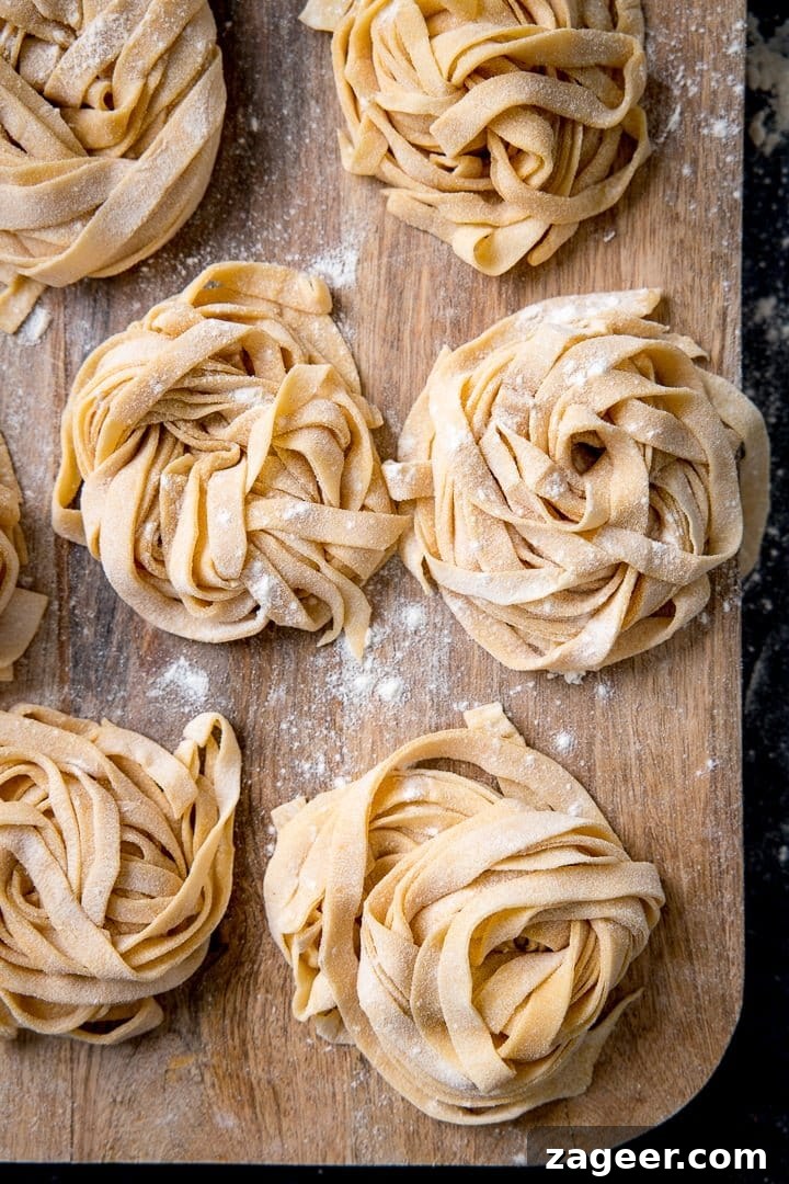Piles of homemade pasta with flour sprinkled on, on wooden board, ready to be cooked or stored.