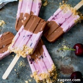 An image of delicious Chocolate Cherry Cheesecake Ice Lollies – a rich chocolate base paired with an easy cherry cheesecake layer and a crumbly cookie base. These popsicles are truly a delightful treat!