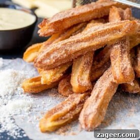 A pile of perfectly baked churros, generously dusted with cinnamon sugar, resting on their side, ready to be enjoyed.