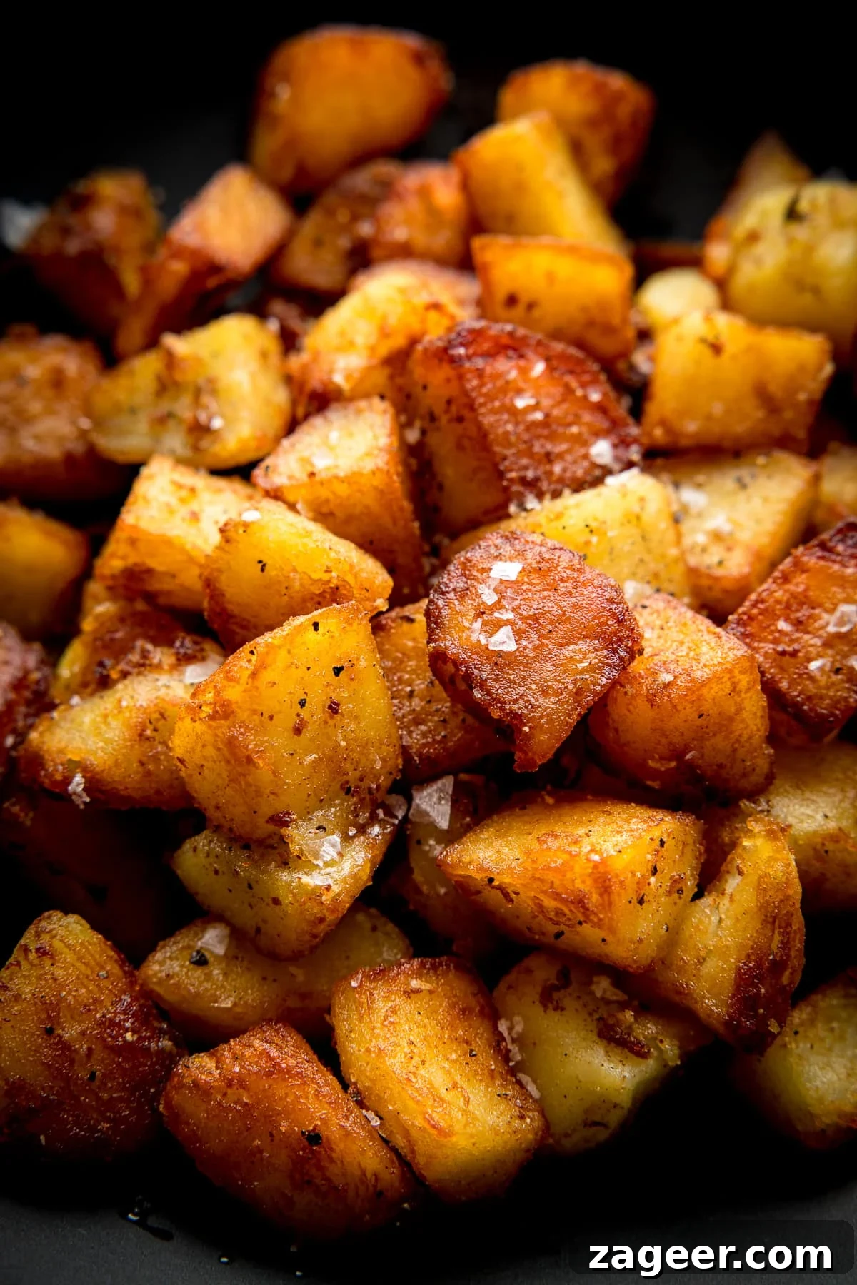 Garlic Sautéed Potatoes 2 Close up image of a pile of crispy saute potatoes in a dark bowl topped with a sprinkling of salt