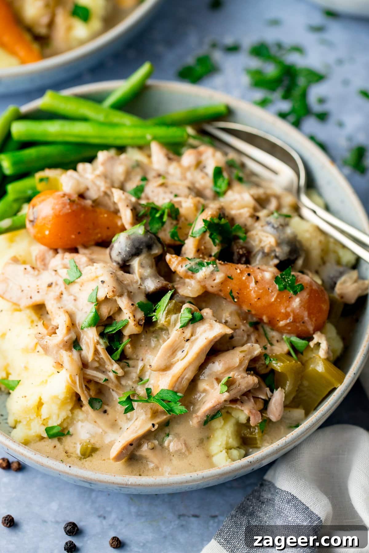 Creamy Slow Cooker Chicken Casserole A bowl of creamy slow cooker chicken casserole with carrots and mushrooms, served alongside mashed potatoes and green beans.