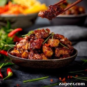 Close up image of bowl of Chinese sticky pork belly pieces. A piece is being taken from the bowl using a pair of chopsticks.