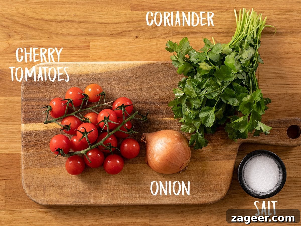 Garden Tomato and Onion Medley 3 Fresh ingredients for Indian Tomato and Onion Salad laid out on a wooden table: cherry tomatoes, a brown onion, fresh coriander, and a pinch of salt.