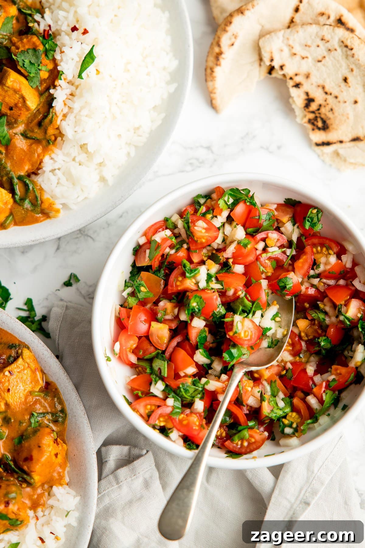 Garden Tomato and Onion Medley 5 Indian Tomato and Onion Salad served in a white bowl alongside a simple chicken curry, boiled rice, and pita bread, creating a complete and balanced Indian meal.