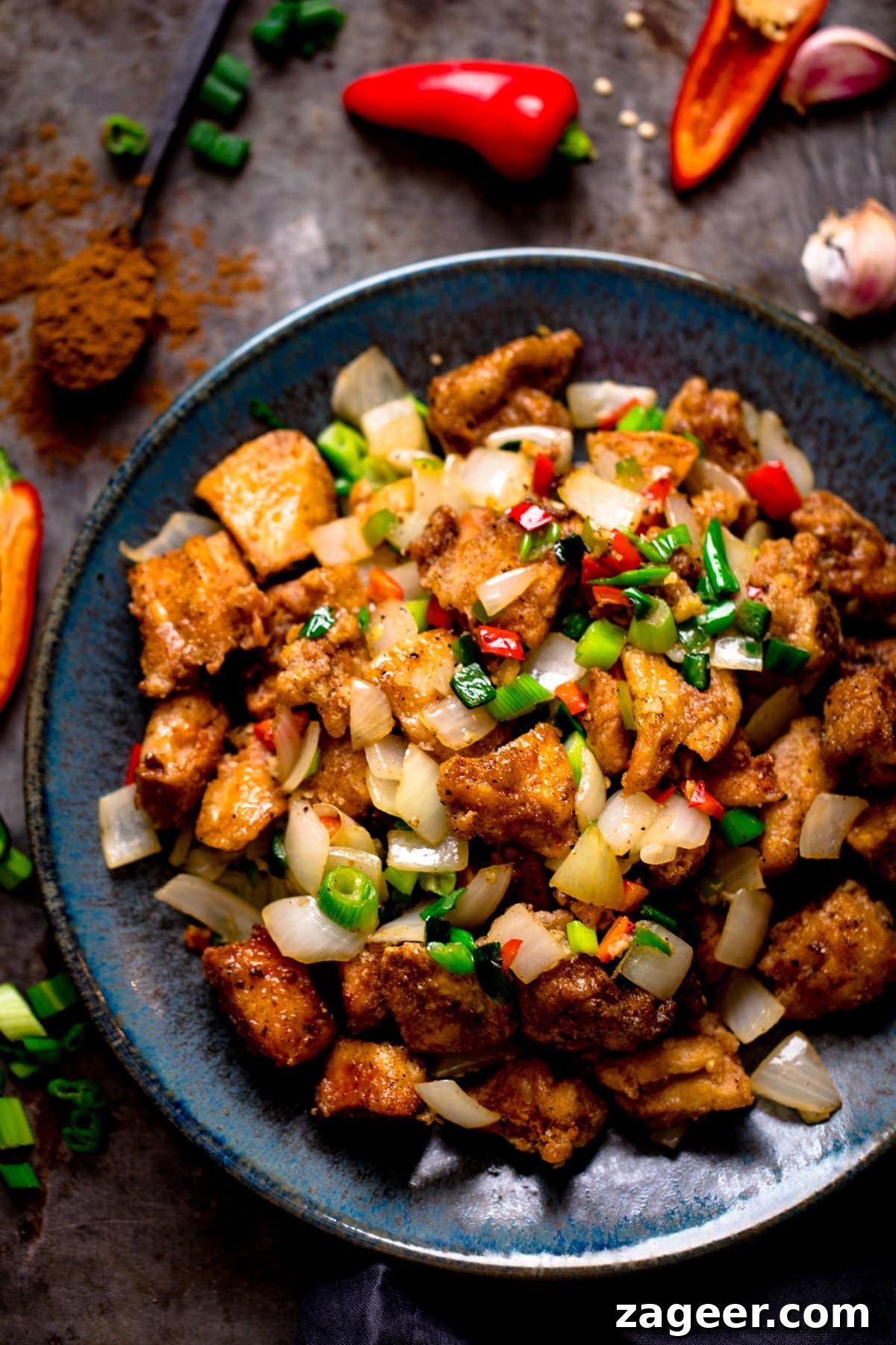 Crispy Salt and Pepper Chicken Bites 2 salt and pepper chicken on a dark blue plate with ingredients scattered around the plate
