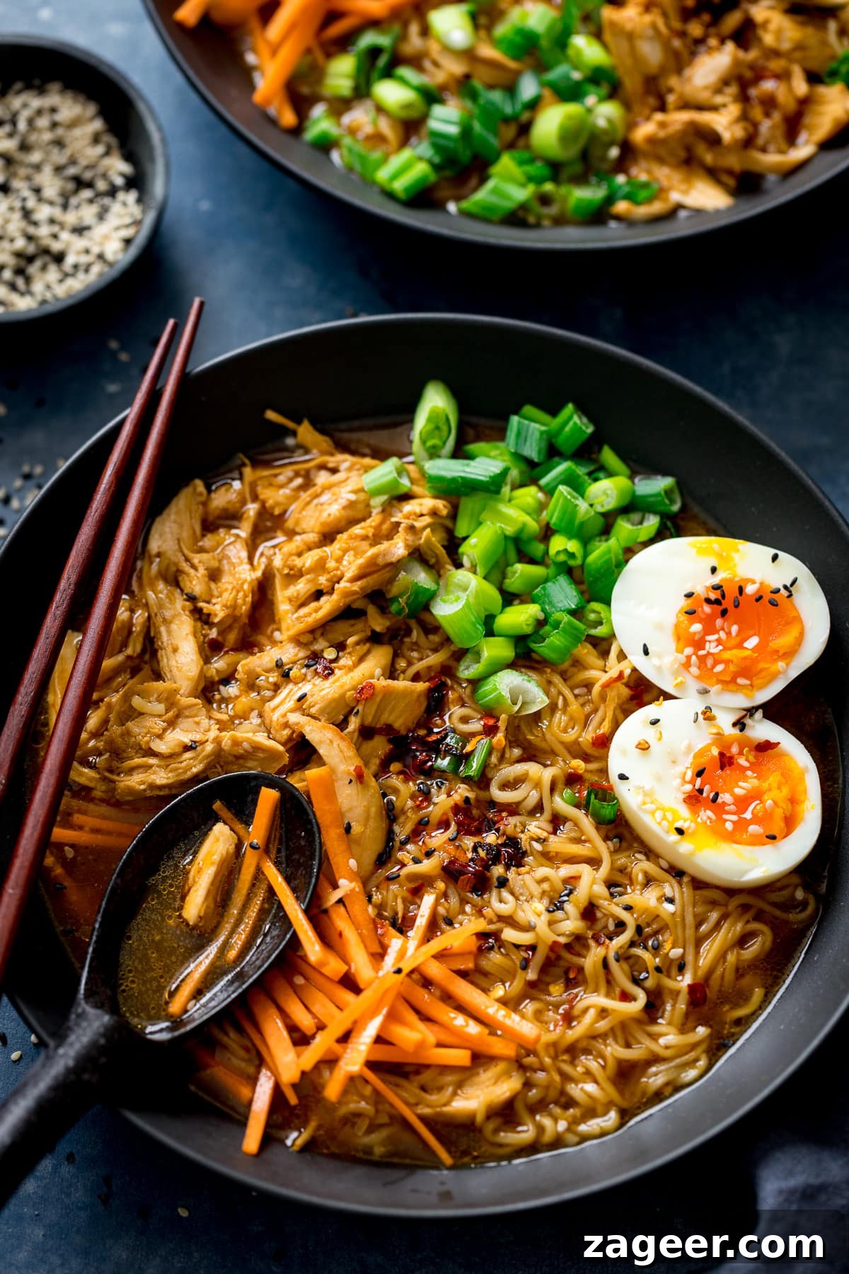 Effortless Chicken Ramen in 20 Minutes 6 A spoonful being taken from a black bowl of chicken ramen, topped with egg, carrots, and spring onions, showcasing the rich broth and noodles.