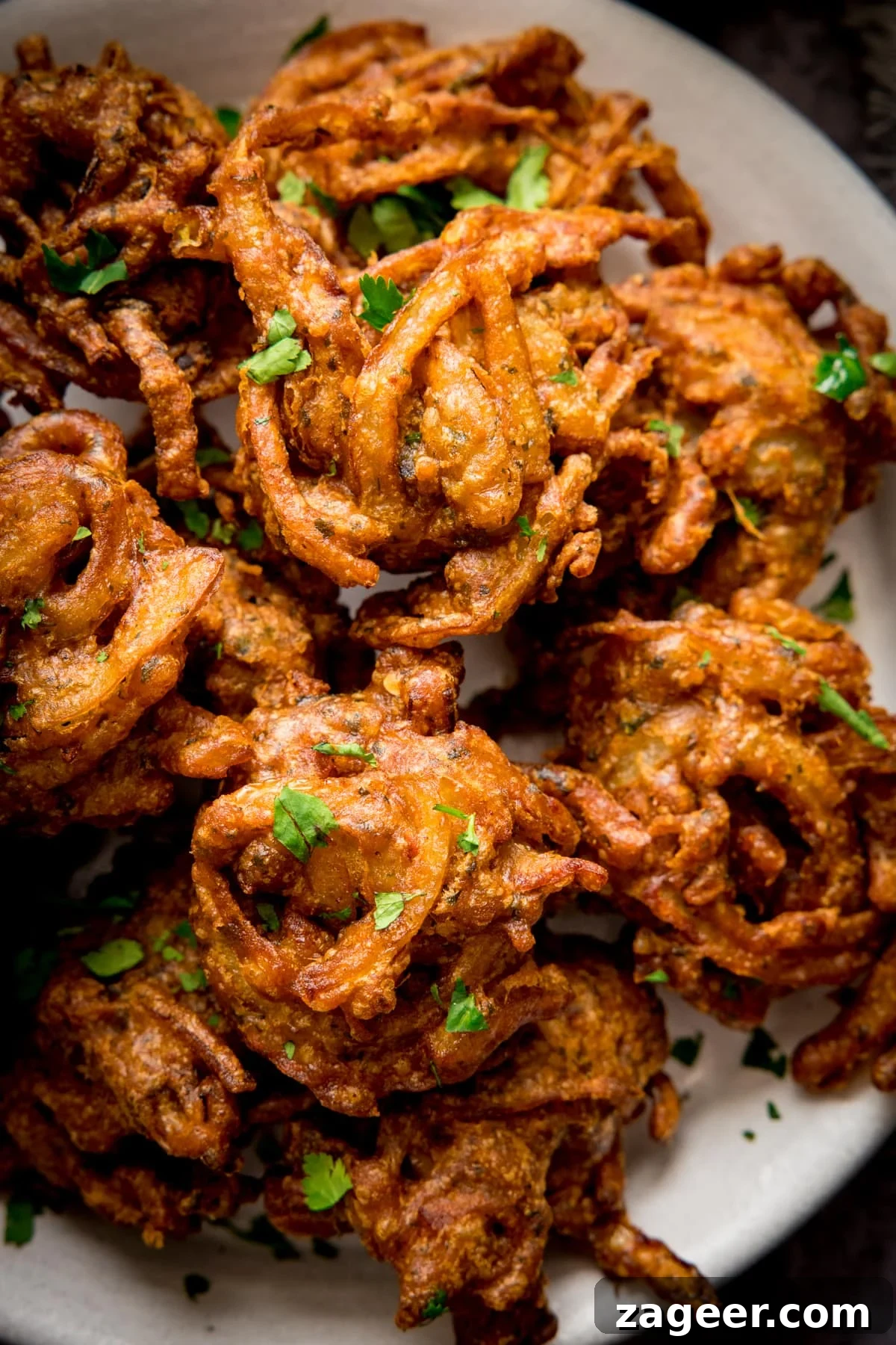 Crispy Golden Onion Bhaji 2 Close-up of golden brown, crispy homemade Onion Bhajis on a white plate, garnished with fresh coriander.