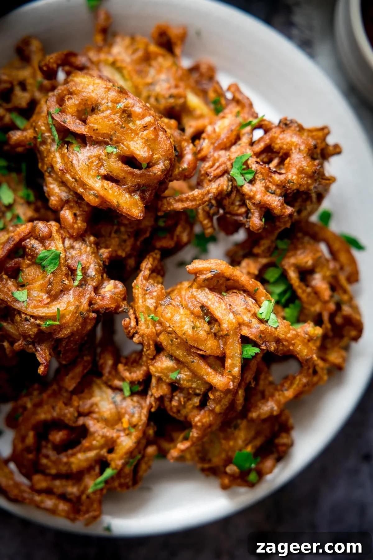 Crispy Golden Onion Bhaji 6 Overhead view of several golden brown Onion Bhajis on a white plate, ready to be served.