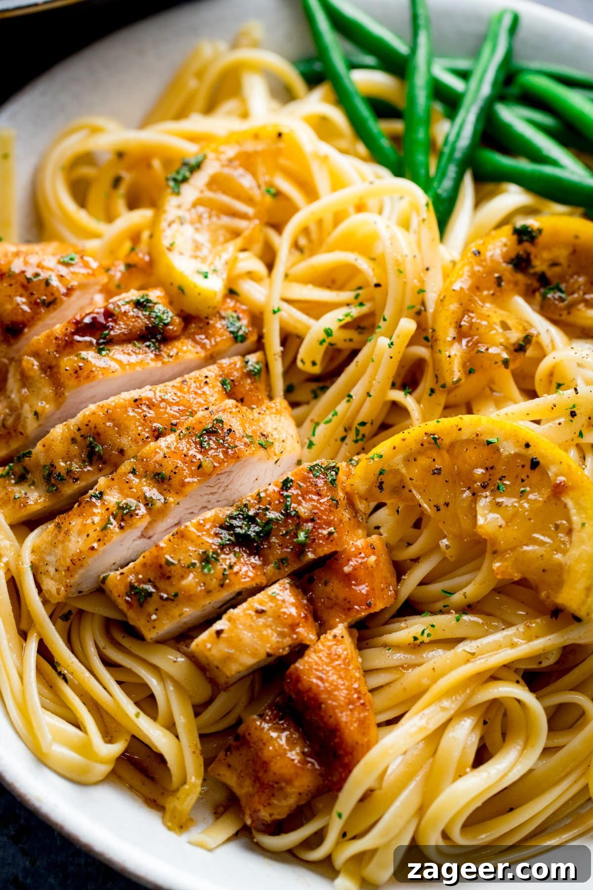 Zesty Honey Glazed Chicken 5 Perfectly sliced honey lemon chicken breast arranged artfully on a bed of linguine pasta, accompanied by vibrant green beans, highlighting its readiness to be served.