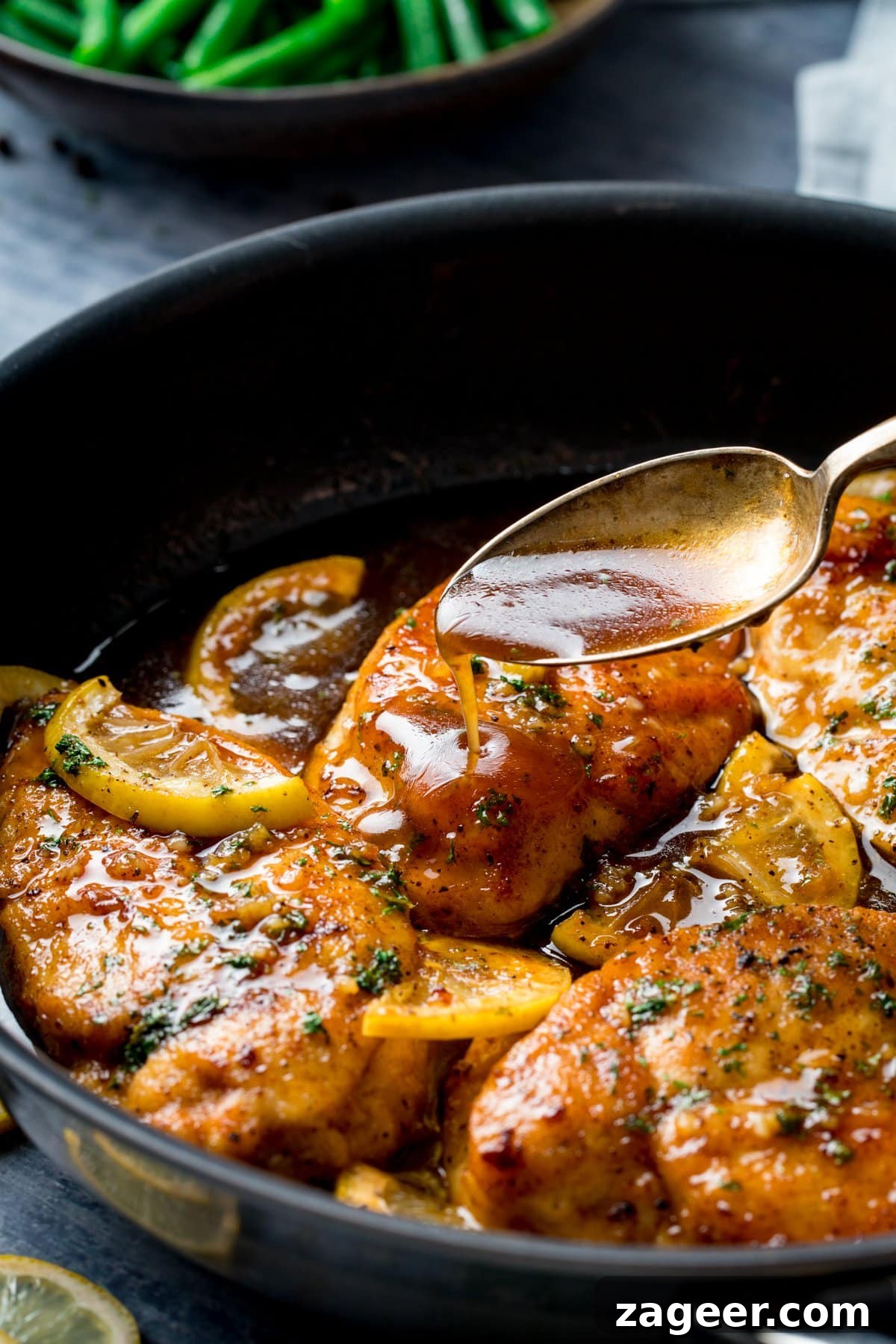 Zesty Honey Glazed Chicken 6 A close-up shot of a spoon drizzling luscious honey lemon sauce over tender chicken pieces directly in the frying pan, showcasing the delicious glaze.
