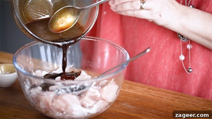 Szechuan Chili Peanut Chicken 5 Pouring marinade over chopped chicken pieces coated with cornflour in a bowl for Kung Pao Chicken.