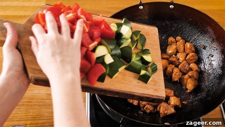 Szechuan Chili Peanut Chicken 7 Adding chopped red bell peppers and zucchini to the wok with cooked chicken for Kung Pao Chicken.
