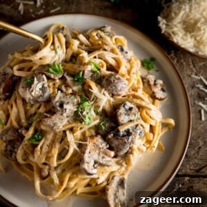 A square shot of creamy mushroom pasta on a white plate with a spoon, on a wooden board with Parmesan in the background