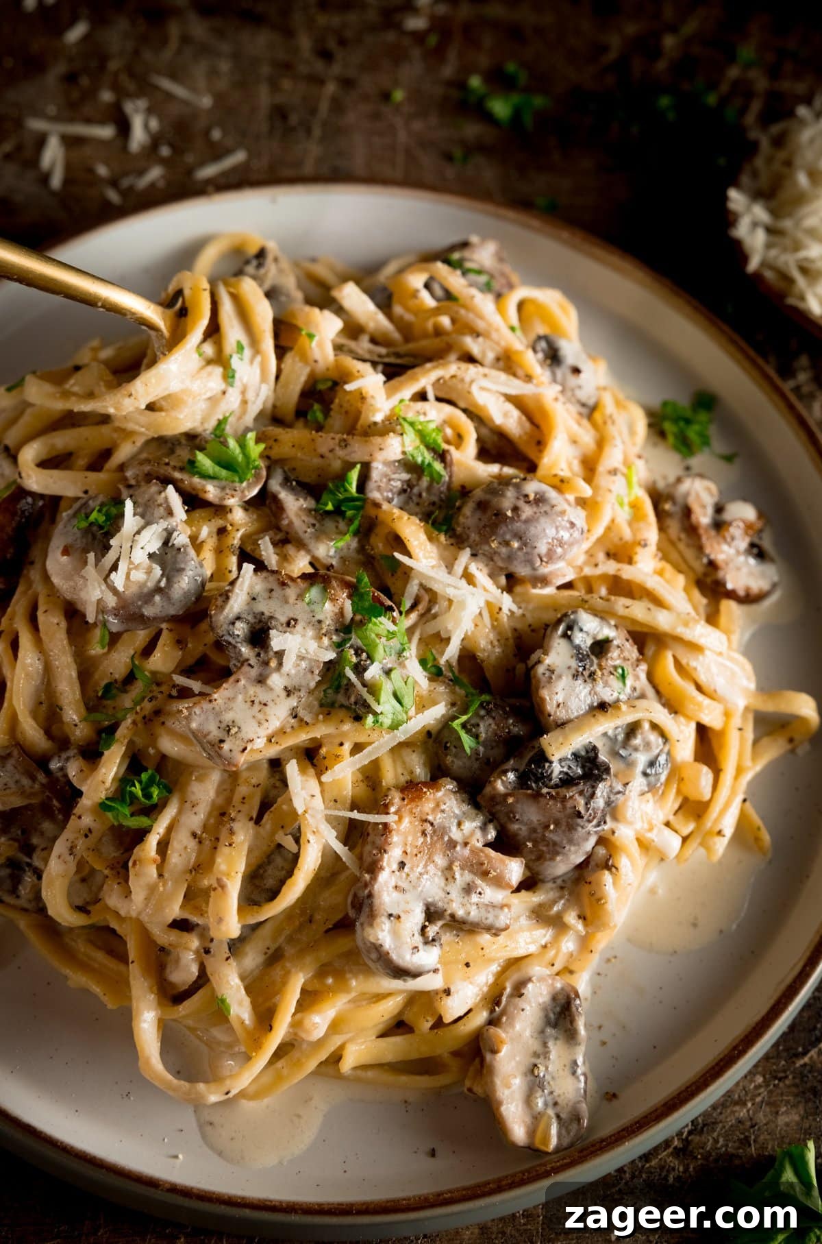 Velvety Mushroom Pasta 5 A white plate piled high with creamy mushroom pasta, featuring a spoon dug in, ready to be enjoyed.