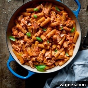 Square image of rigatoni and salmon in creamy tomato sauce in a blue cast iron pan on a wooden table.