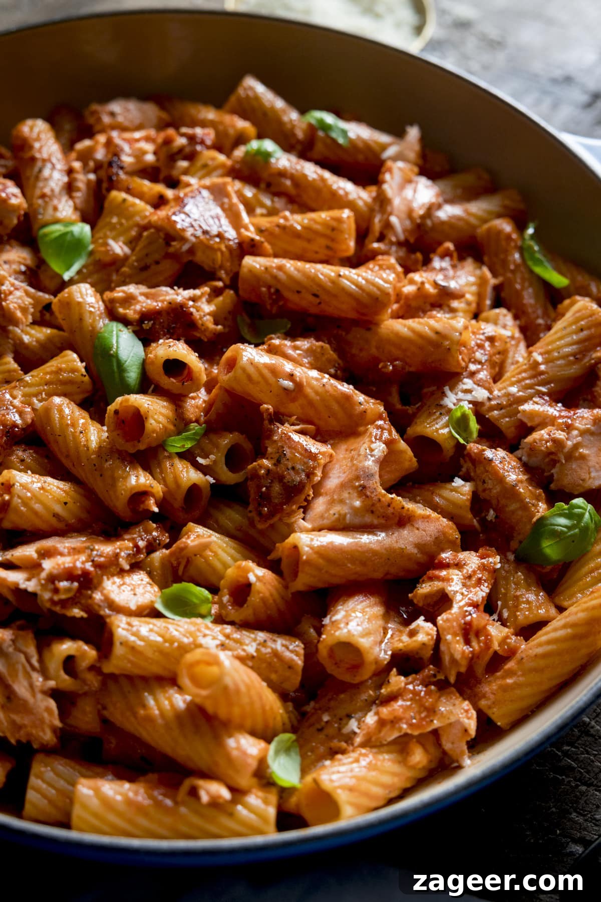 Blush Salmon Rigatoni 4 Close up of creamy tomato salmon rigatoni in a pan, topped with a sprinkling of basil leaves.
