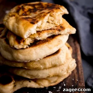 Homemade Peshwari Naan: Sweet & Fluffy Indian Bread 5 Close up of a stack of peshwari naan breads on a dark wooden board against a blue background. There is a blue napkin in shot. The top naan has been broken into two to show the filling.
