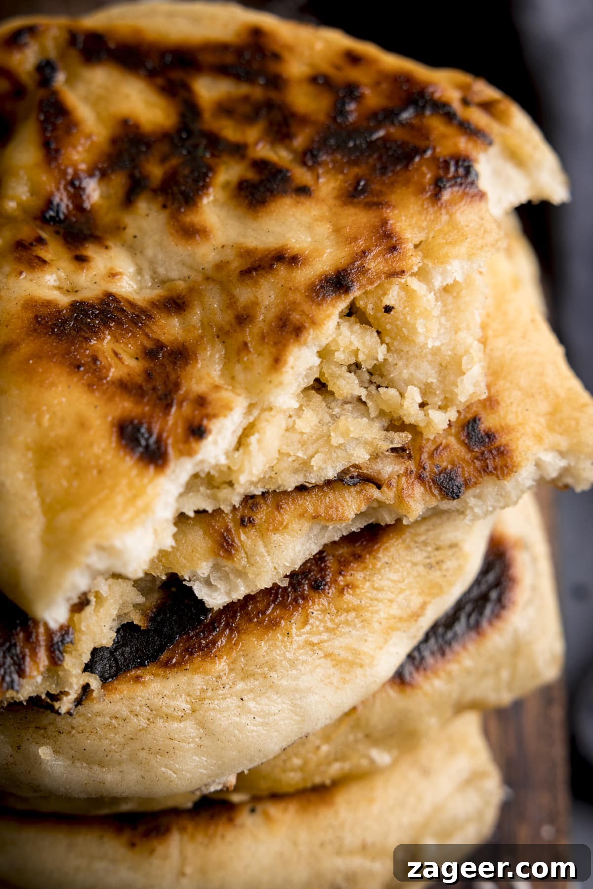 Homemade Peshwari Naan: Sweet & Fluffy Indian Bread 3 Close up overhead image of a stack of peshwari naan breads on a wooden board. The top naan has been torn in two, to reveal the filling.
